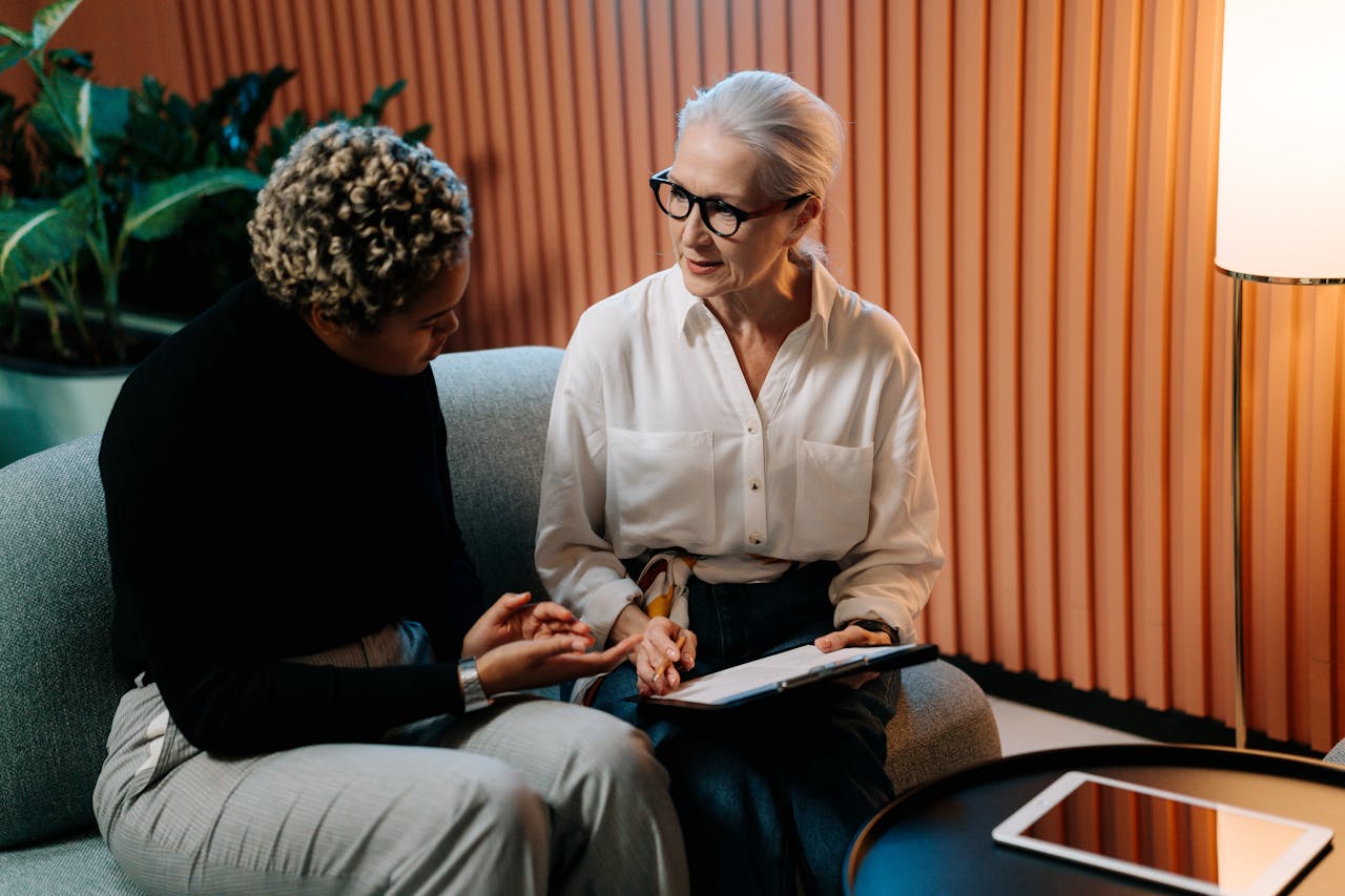 about-01 Two professional women engaged in a business discussion indoors with documents.